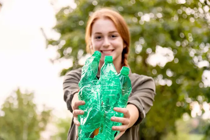 Smiling female volunteer showing green plastic bottles in garden