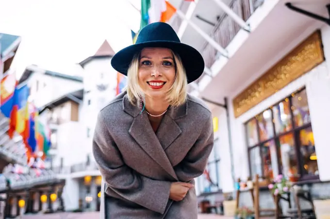 Smiling beautiful woman wearing hat and coat bending in city