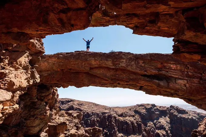 Young man with arms outstretched standing on natural rock arch, Gran Canaria, Spain