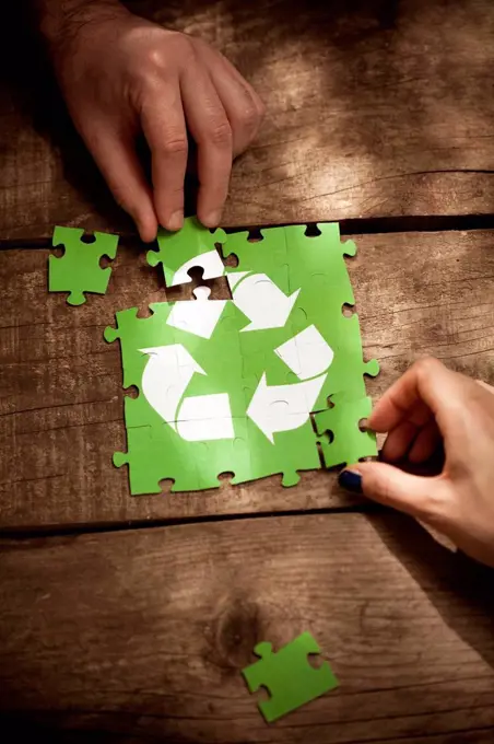 Friends joining recycling symbol jigsaw puzzle on table