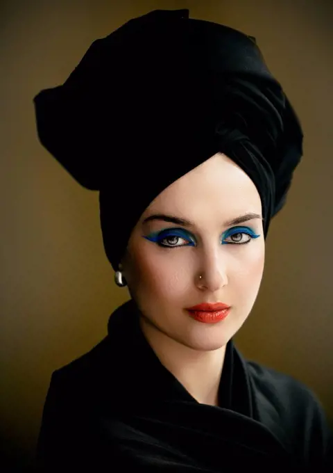 Beautiful woman with eye make-up wearing black turban against brown background