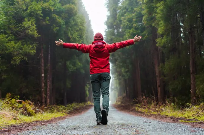 Man with arms outstretched walking on road at forest