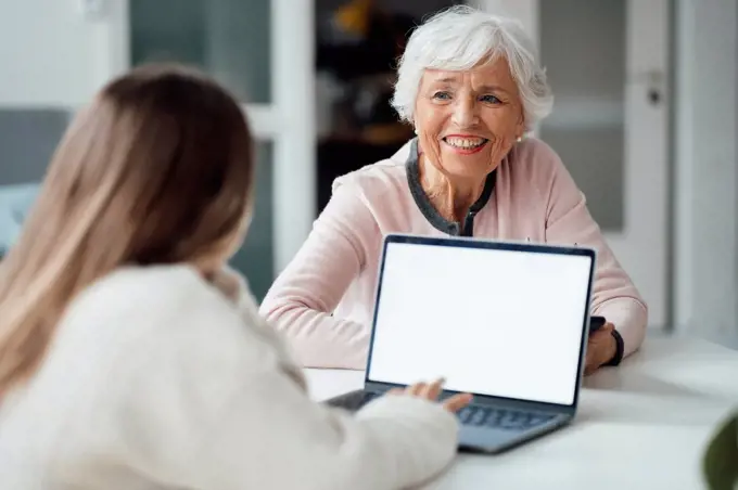 Woman looking at girl using laptop on table
