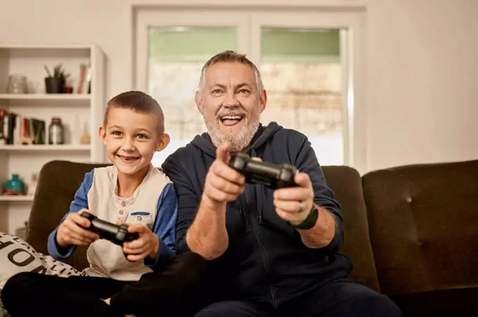 Playful grandfather playing video game with grandson at home