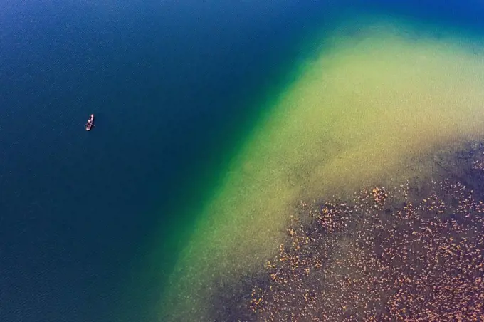 Drone view of fishing boat in front of reed belt stretching along shore of Irrsee lake in autumn