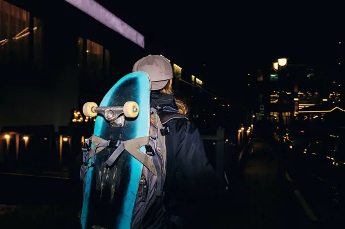Man with backpack carrying skateboard at night