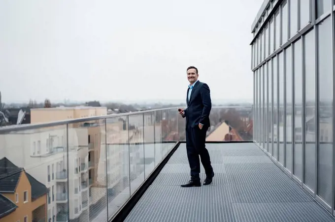 Smiling businessman with hand in pocket standing on balcony