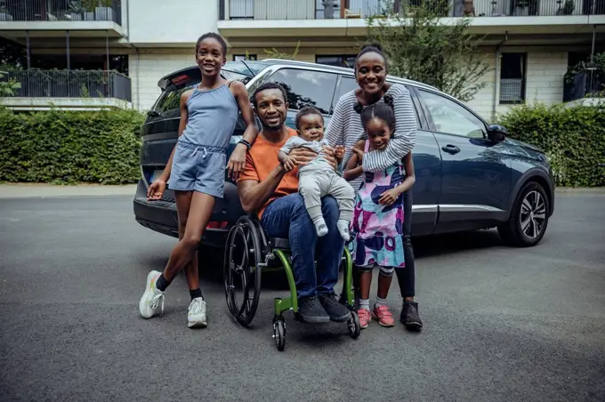 Father sitting on wheelchair by family on road