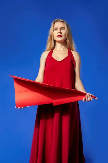 Woman holding red paper airplane standing against blue background
