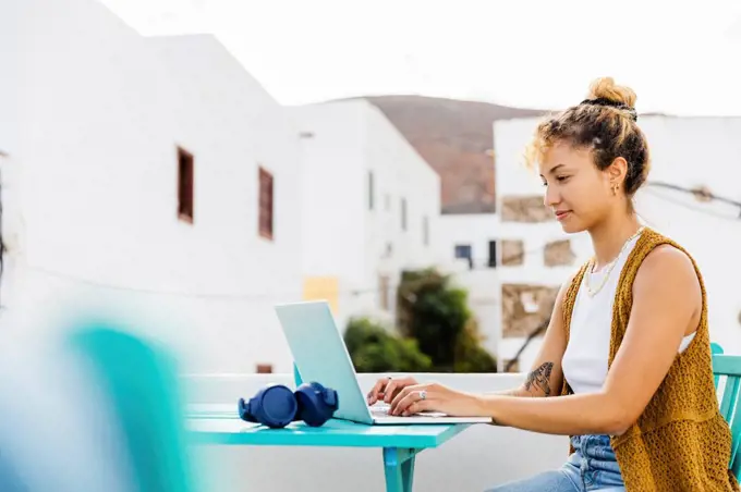 Smiling young freelancer using laptop sitting at table on rooftop