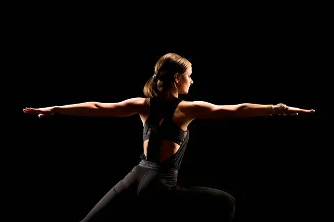 Woman with arms outstretched practicing yoga against black background