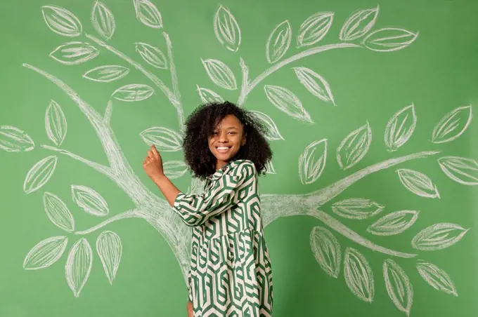 Smiling woman standing in front of tree drawing on green wall
