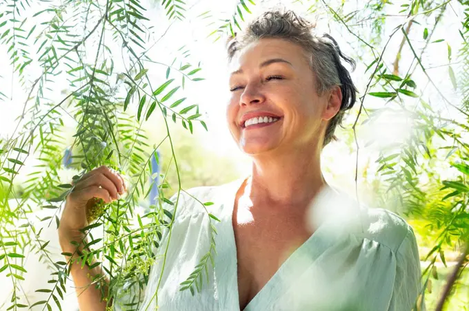 Smiling woman with eyes closed standing amidst twigs in garden