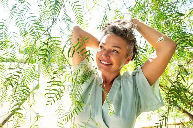 Smiling mature woman standing amidst twigs on sunny day