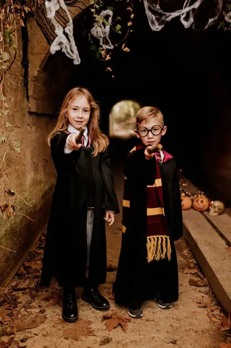 Boy and girl in witch and wizard costumes pointing magic wands