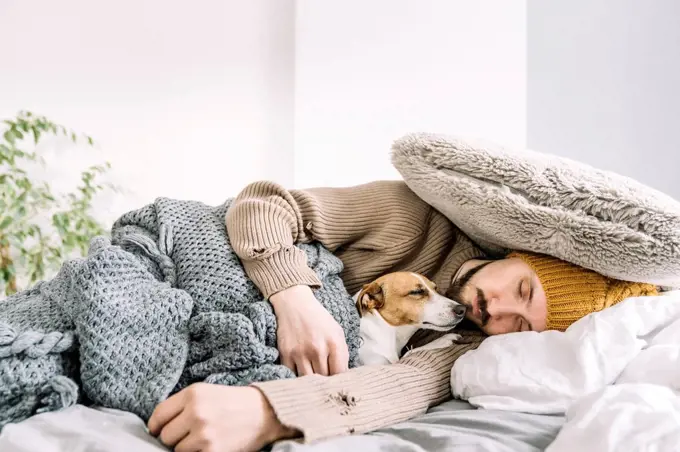 Exhausted man sleeping fully dressed in bed with dog