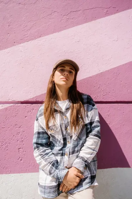 Young woman wearing cap standing in front of pink wall