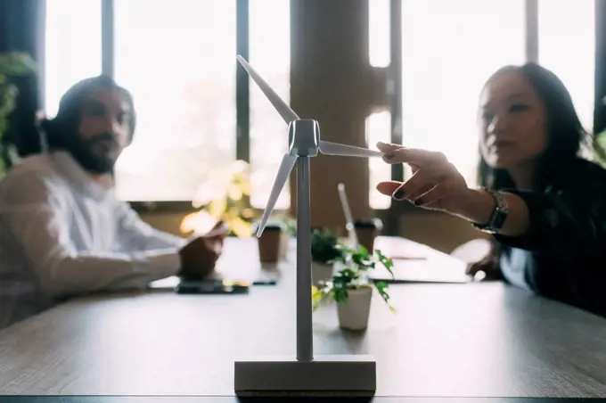 Businesswoman discussing over wind turbine model with colleague at work place