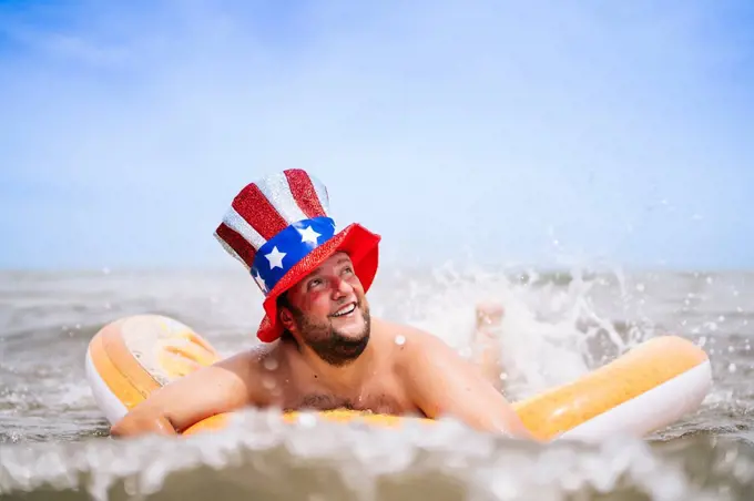 Carefree man wearing Uncle Sam hat swimming with pool raft in sea