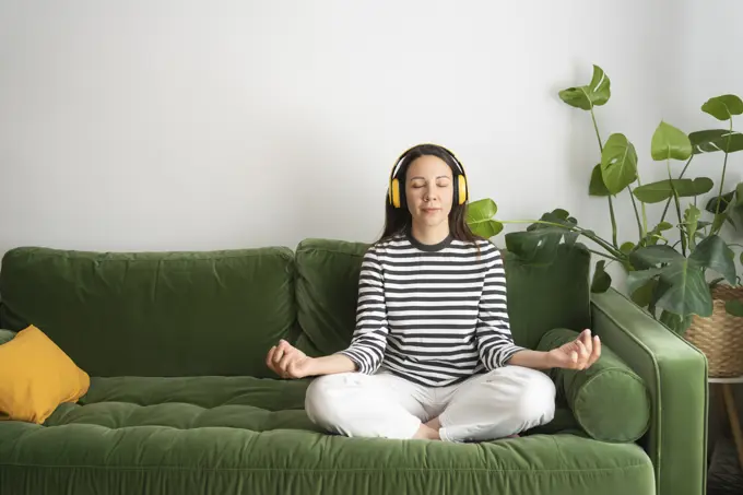 Woman listening music and meditating on sofa at home