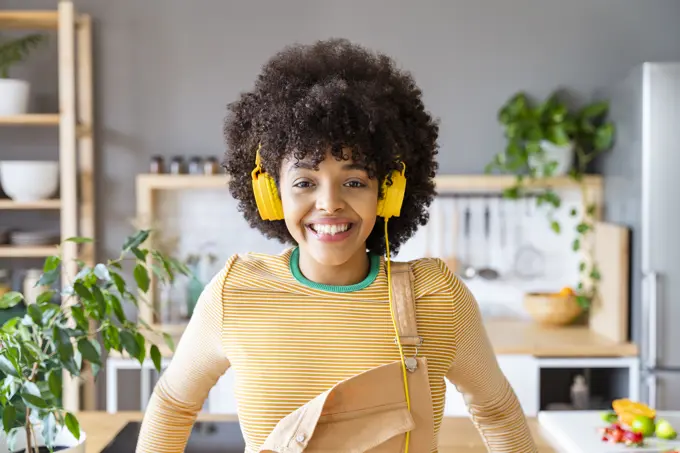Happy woman listening music through yellow headphones at home