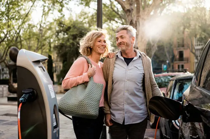 Smiling mature couple charging electric car