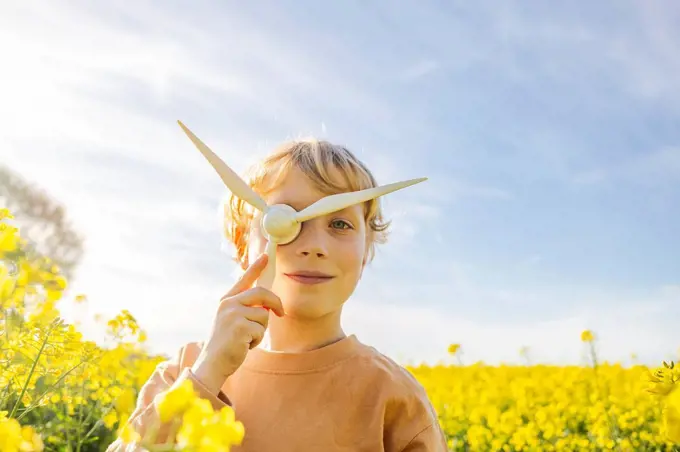 Boy playing with wind turbine model at rapeseed field