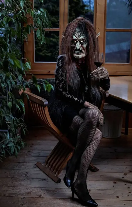 Woman wearing witch costume sitting with wineglass on chair at horror house