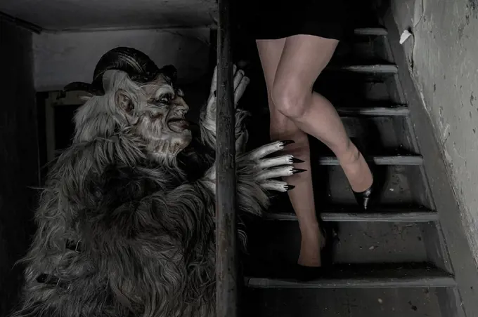 Man in krampus costume trying to scare woman moving down on steps at horror house