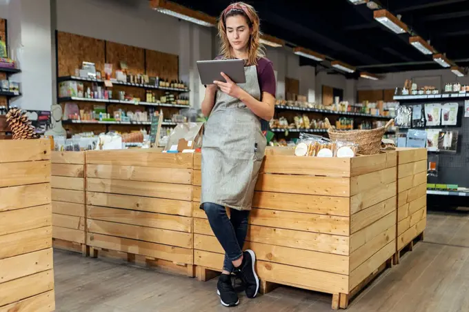 Store owner using tablet PC leaning on crate at organic market