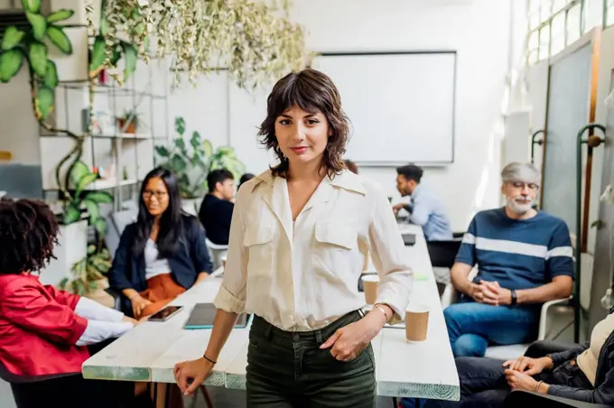 Confident businesswoman with colleagues in background at workplace