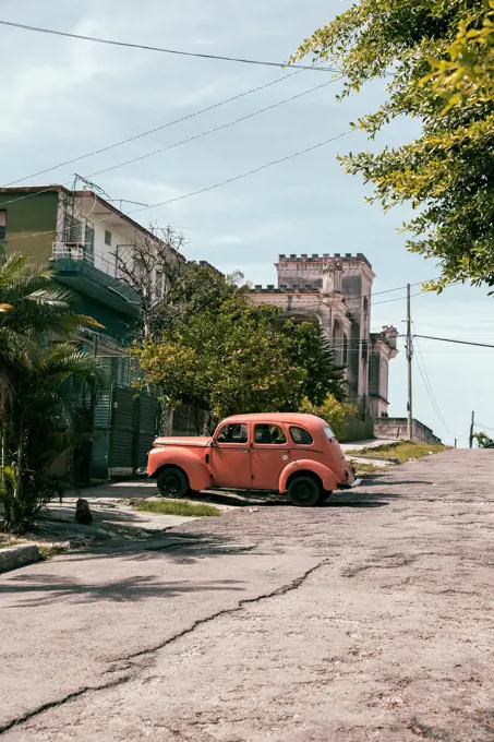 Cuba, Havana, Peach colored vintage car parked along street in La Vibora neighborhood