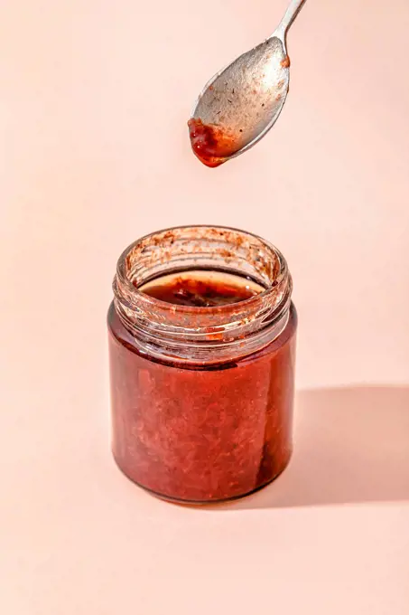 Homemade strawberry jam with spoon over peach background