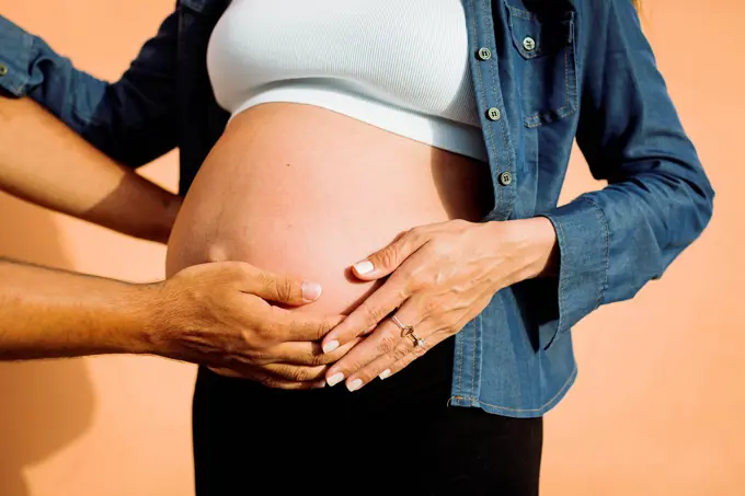 Couple with hands on stomach of pregnant woman in front of wall