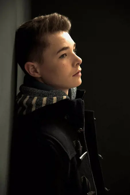 Profile of serious looking teenager leaning against black wall