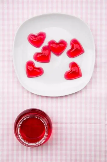 Plate of red hearts shaped of cherry jelly and preserving jar of cherry jelly on checkered cloth