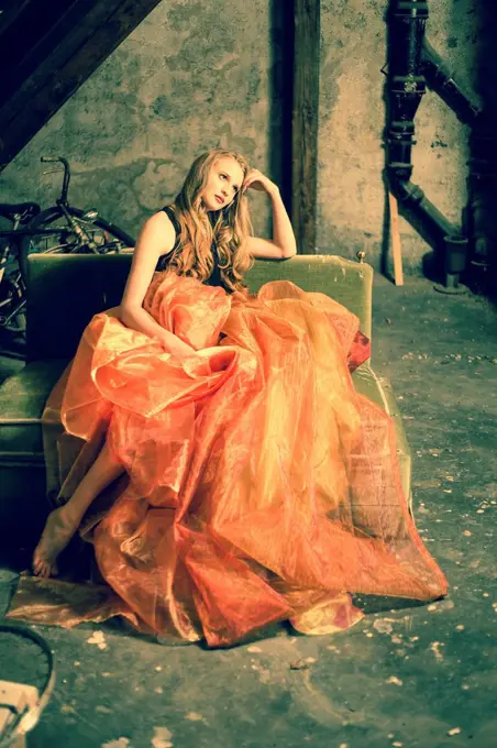 Portrait of young woman sitting at attic wearing orange skirt