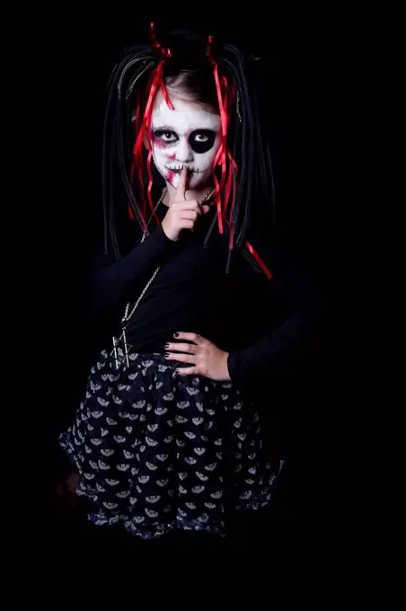 Girl with finger on mouth masquerade as devil in front of black background