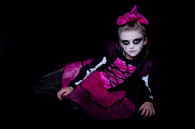 Little girl masquerade as modern undead witch lying in front of black background