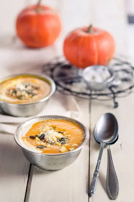 Bowls of Exotic pumpkin soup with coconut milk and coconut flakes on white wood