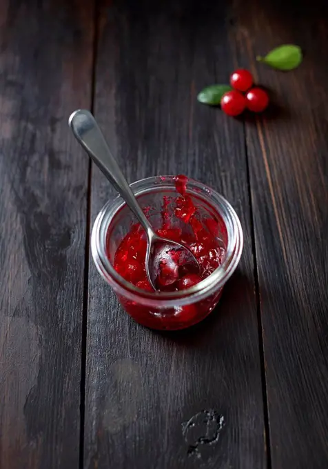 Cranberry sauce in a glass with spoon on dark wood