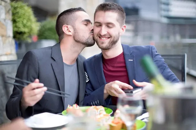 Gay couple kissing and eating sushi at outdoor restaurant
