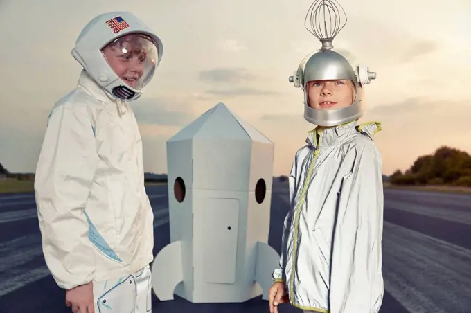 Two boys dressed up as spacemen standing at cardboard rocket