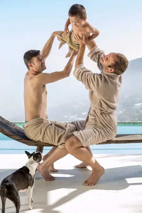 Gay couple playing with baby at the poolside