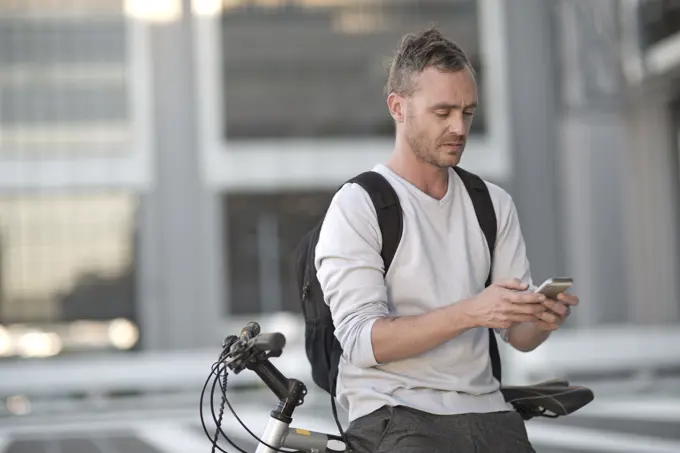 Blone man on bicycle using smart phone