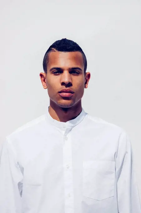Portrait of young man with shaved hair wearing white shirt in front of white background