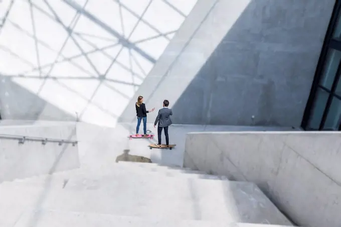 Two business people standing on skateboards in modern architecture