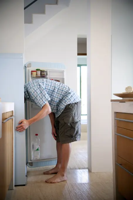 Young man standing in the kitchen searching something in the fridge