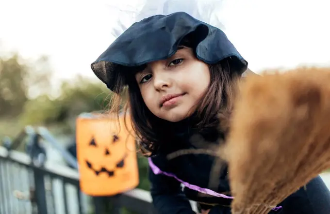 Portrait of little girl masquerade as a witch with halloween lantern and broom