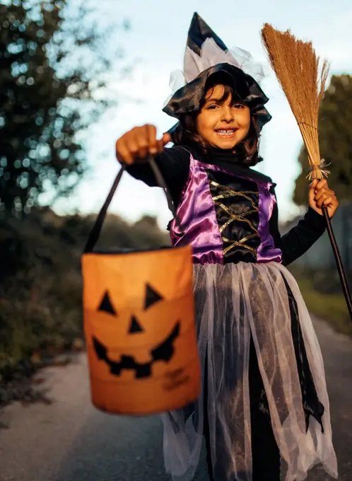 Portrait of little girl masquerade as a witch with halloween lantern and broom